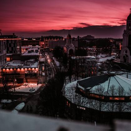 Explore The Enchanting Cityscape Under A Vivid Sunset Sky, Showcasing Illuminated Streets And Buildings.