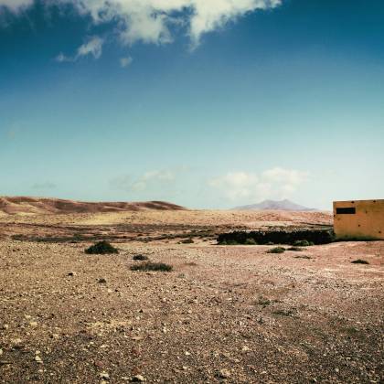 A Solitary Concrete Bunker Stands Isolated In A Barren Desert Landscape Under A Clear Sky.