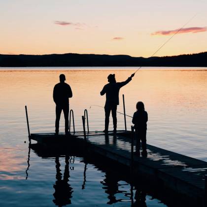A Serene Scene Of A Family Fishing Together On A Lake Dock At Sunset, Creating Silhouettes On The Water.