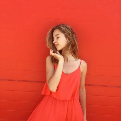 Portrait Of A Young Woman Wearing A Stylish Red Dress, Posing Gracefully Against A Matching Red Background.
