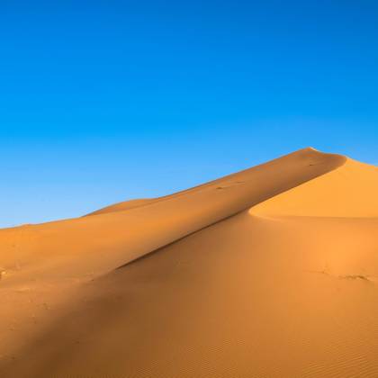A Breathtaking View Of Golden Sand Dunes Contrasted Against A Vibrant Blue Sky In A Desert Landscape.