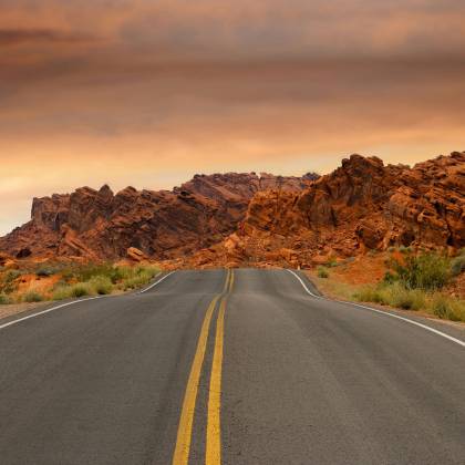 A Scenic Highway Winds Through Dramatic Red Desert Rock Formations Under A Colorful Sunset Sky.